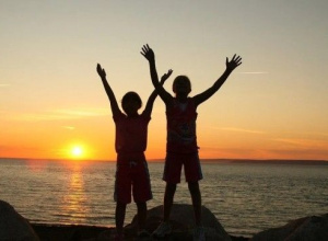 zdiecie dzieci na tle zachodu słońca nad morzem, sylwetki dzieci sa czarne